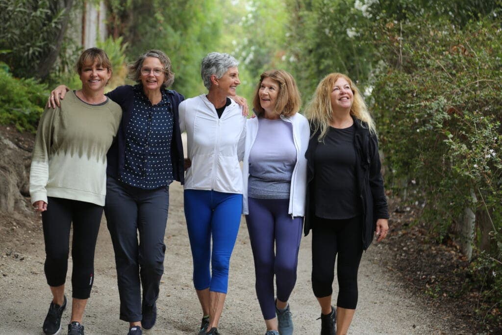 5 women walking arm and arm surrounded by nature