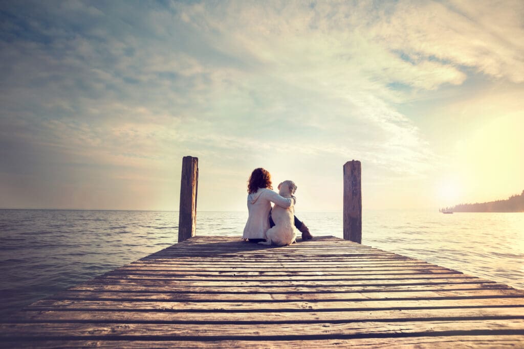 woman embracing sweetly his dog while looking the view of lake