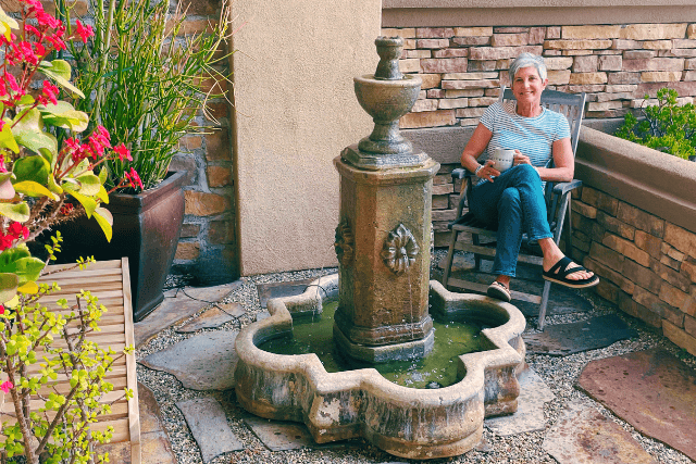 grey haired woman sipping coffee by a water fountain