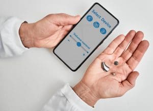 Doctor audiologist showing smartphone app for adjusting hearing aid holding smartphone