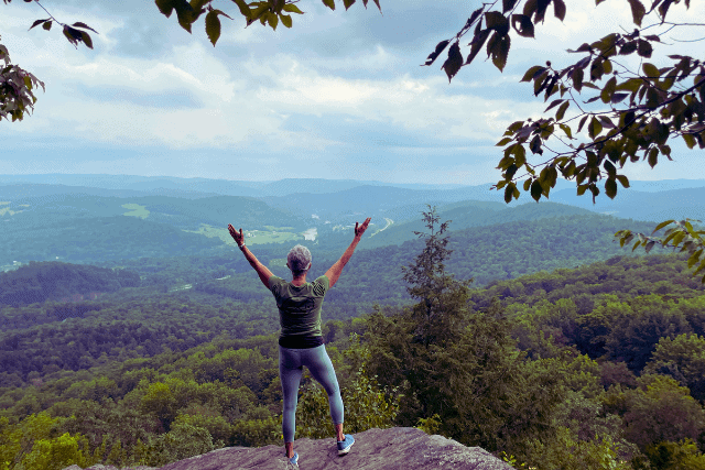 female standing at mountain top with arms extended