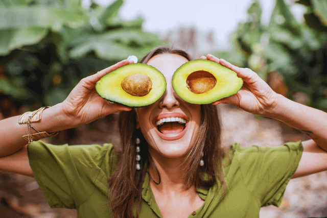 Woman holding avocado halves to her eyes like glasses
