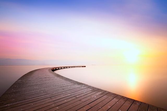Serene wooden pier extending into calm water at sunrise or sunset.